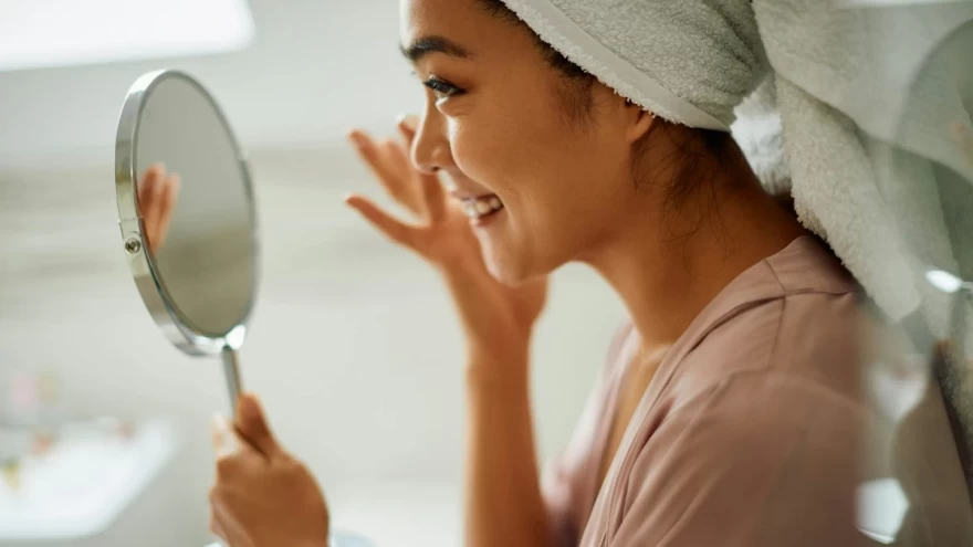γυναίκα εφαρμόζει κρέμα προσώπου μπροστά σε καθρέφτη