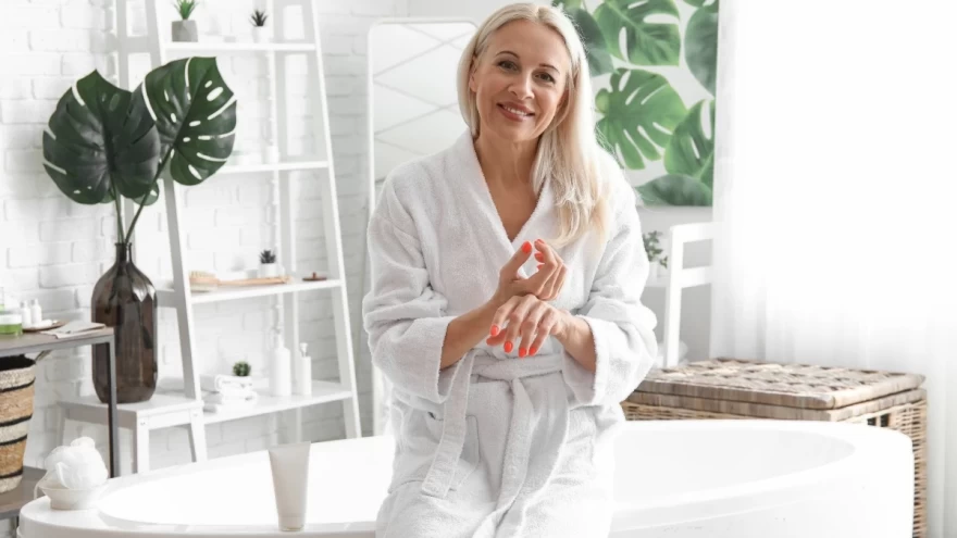 γυναίκα στο μπάνιο με μπουρνούζι εφαρμόζει κρέμα