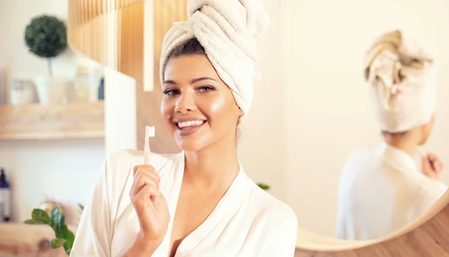 γυναίκα με μπουρνούζι βουρτσίζει τα δόντια της