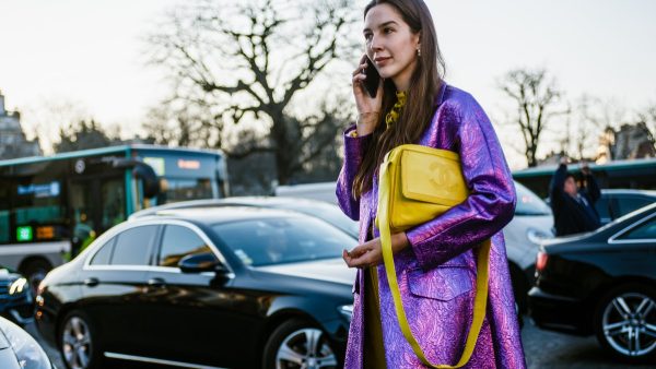 Γυναίκα με κίτρινη τσάντα και μοβ παλτό