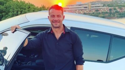 Ο Γιώργος Αγγελόπουλος μπροστά από λευκό αυτοκίνητο με φόντο το ηλιοβασίλεμα