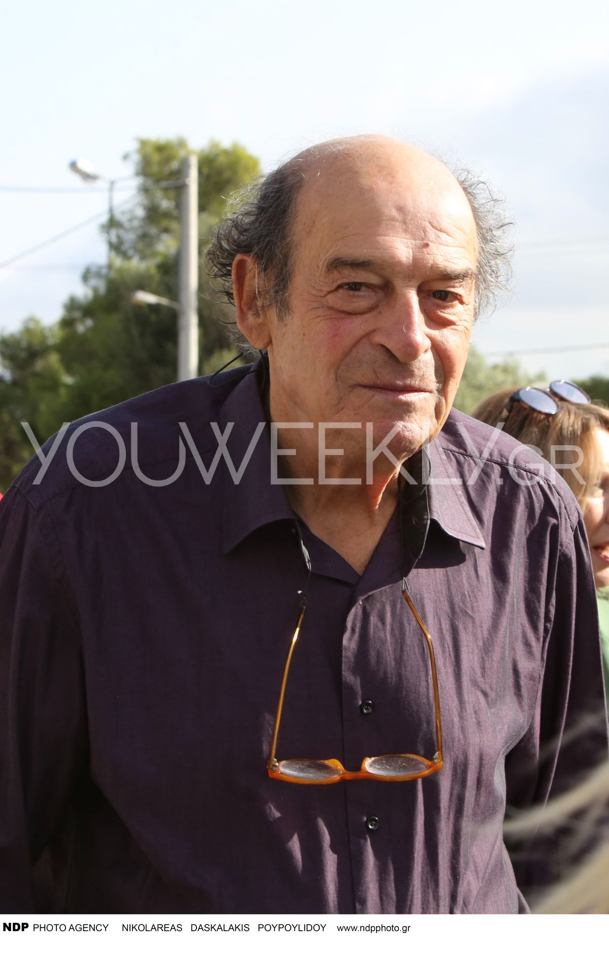 Ο Μανούσος Μανουσάκης με μωβ πουκάμισο και τα γυαλιά κρεμασμένα σε έξοδό του