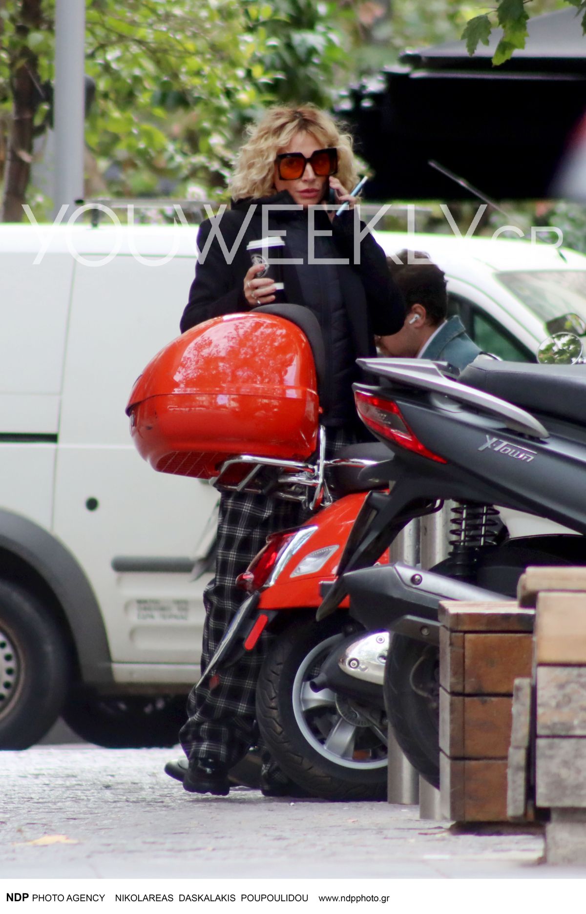 Η Ελεωνόρα Ζουγανέλη δίπλα από το κόκκινο μηχανάκι της με τον καφέ στο χέρι