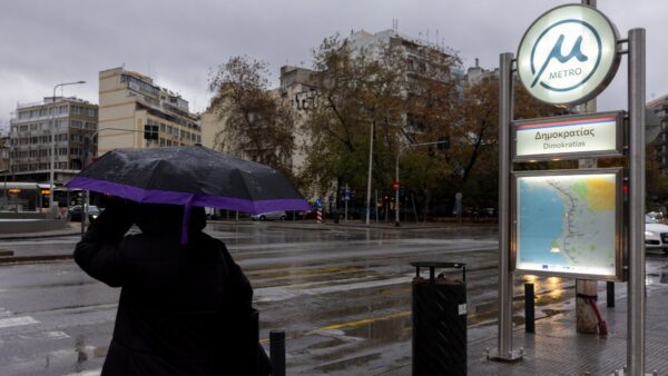 Βροχερή μέρα και μία κυρία με ομπρέλα δίπλα σε σταθμό μετρό