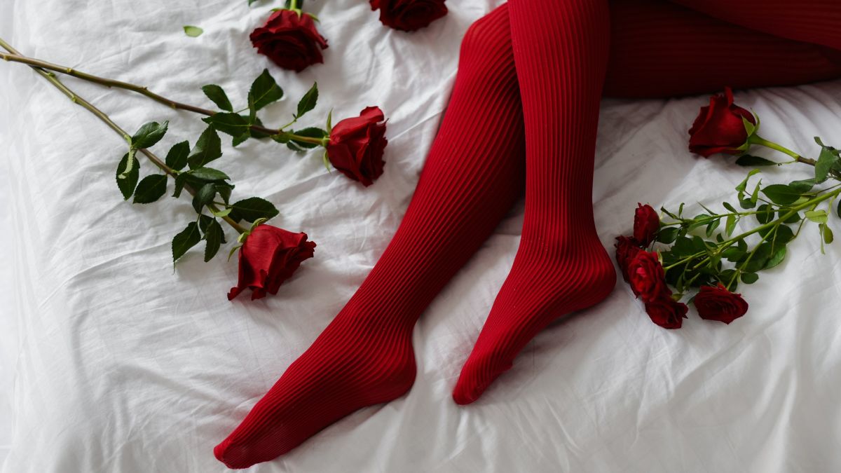 Μια γυναίκα ξαπλωμένη στο κρεβάτι φορώντας κόκκινο καλτσόν