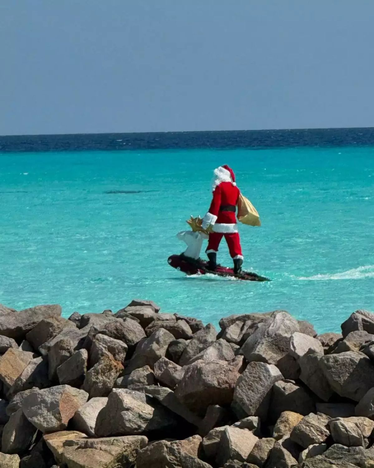 Ένας άντρας ντυμένος Άγιος Βασίλης με σανίδα του σερφ στη θάλασσα