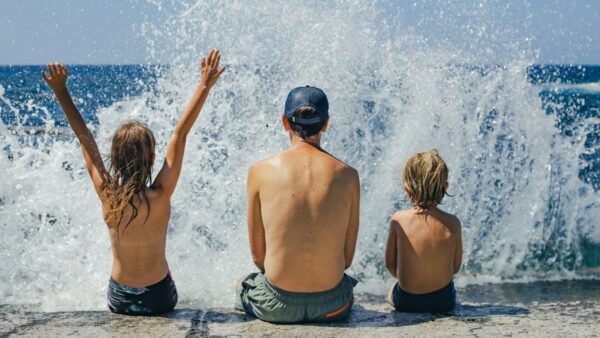 ένας πατέρας με δυο γιους παίζουν με τα κύματα της θάλασσας