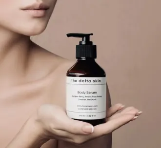 Μπουκάλι body serum Delta Skin, κρατημένο σε γυναικείο χέρι πάνω σε ουδέτερο μπεζ φόντο