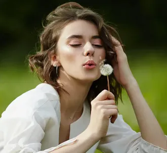 Γυναίκα σε εξωτερικό χώρο φυσά απαλά ένα λουλούδι πικραλίδας